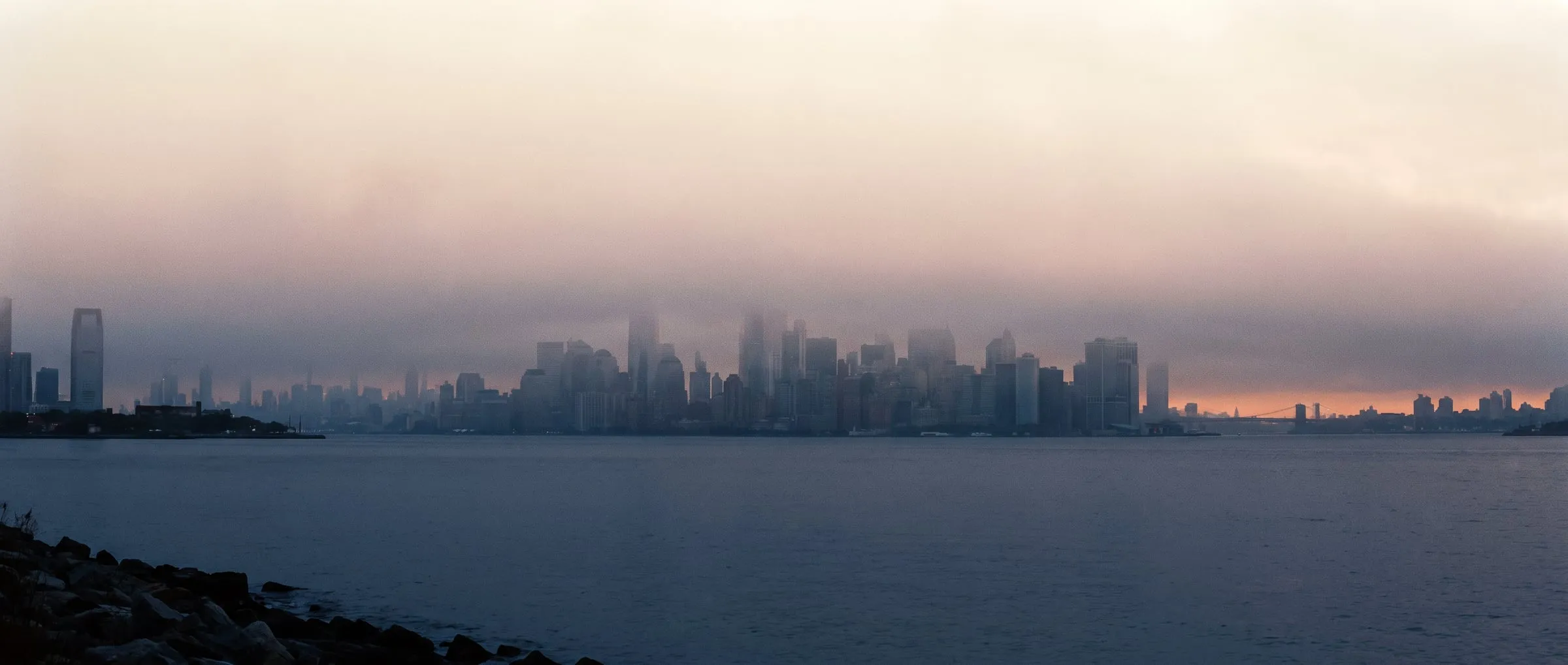 Lower Manhattan at first light, seen across the water through morning fog.