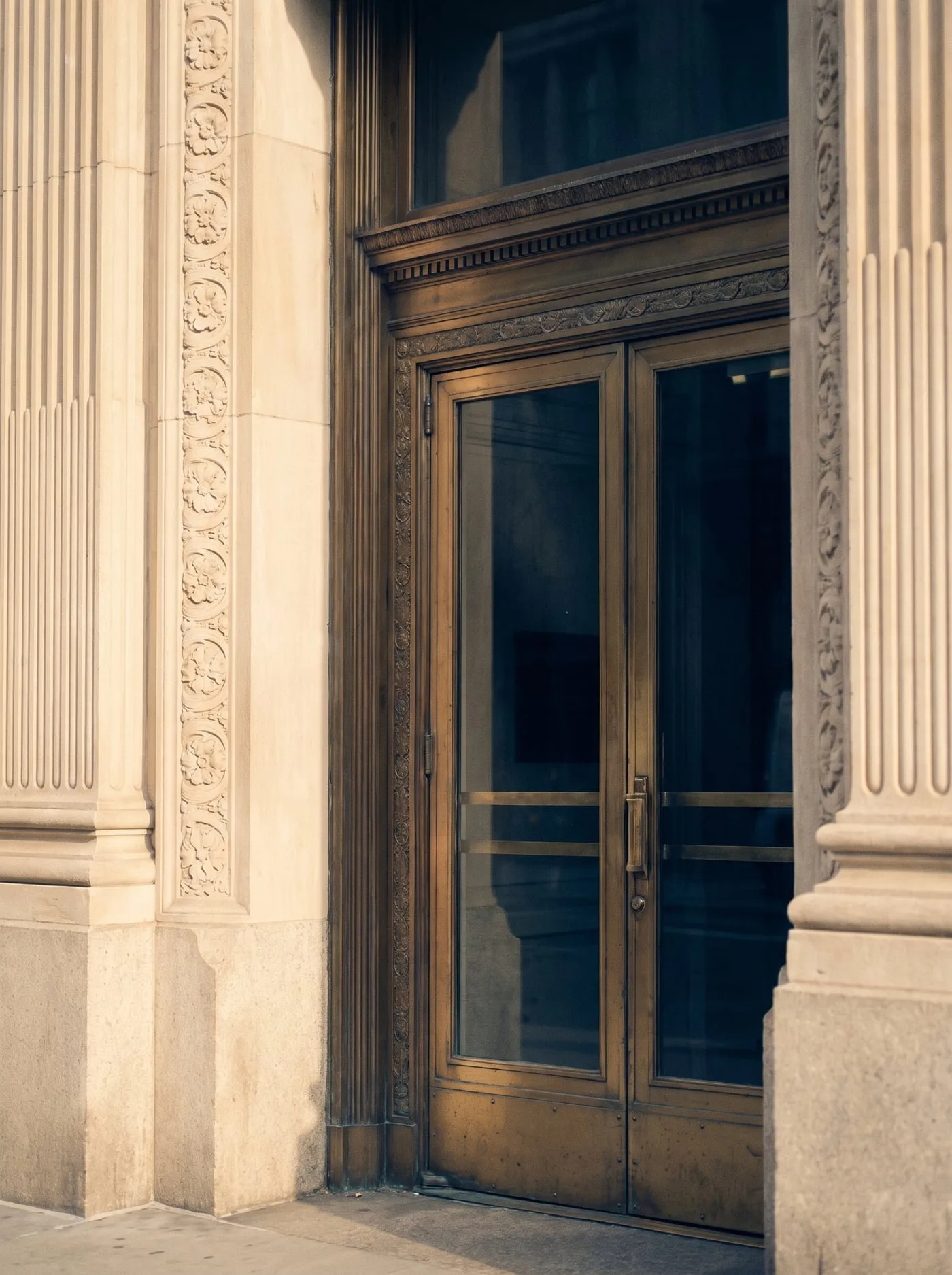 The unmarked brass door of a limestone building in late light.